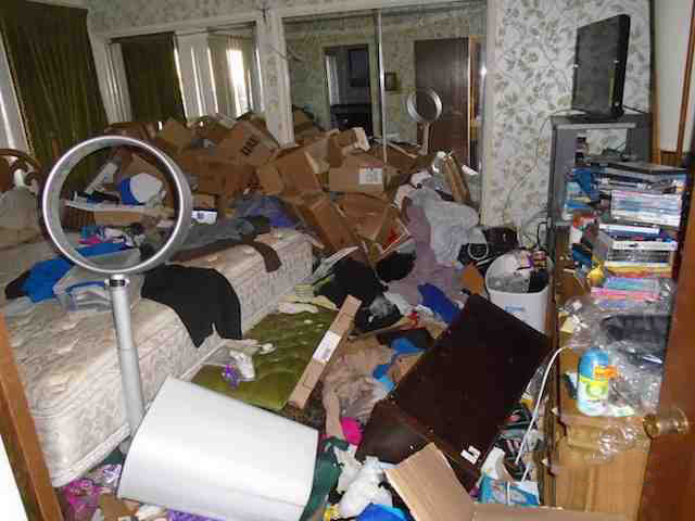 before picture of a hoarded master bedroom with boxes and trash all over the bedroom and bed