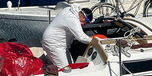 biohazard technician exiting a sailboat cabin with red bags on the deck