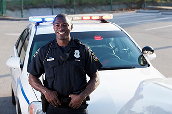 law enforcement officer smiling and standing in front of his patrol car