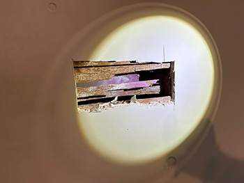 flashlight shining on hole in drywall with purple residue from a tear gas canister