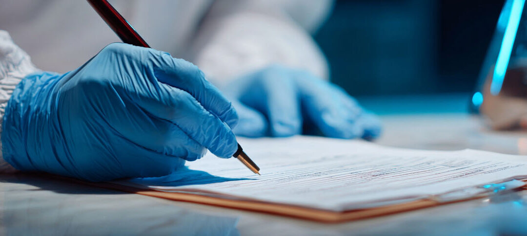 the gloved hand holding a pen of a medicolegal investigator writing a report