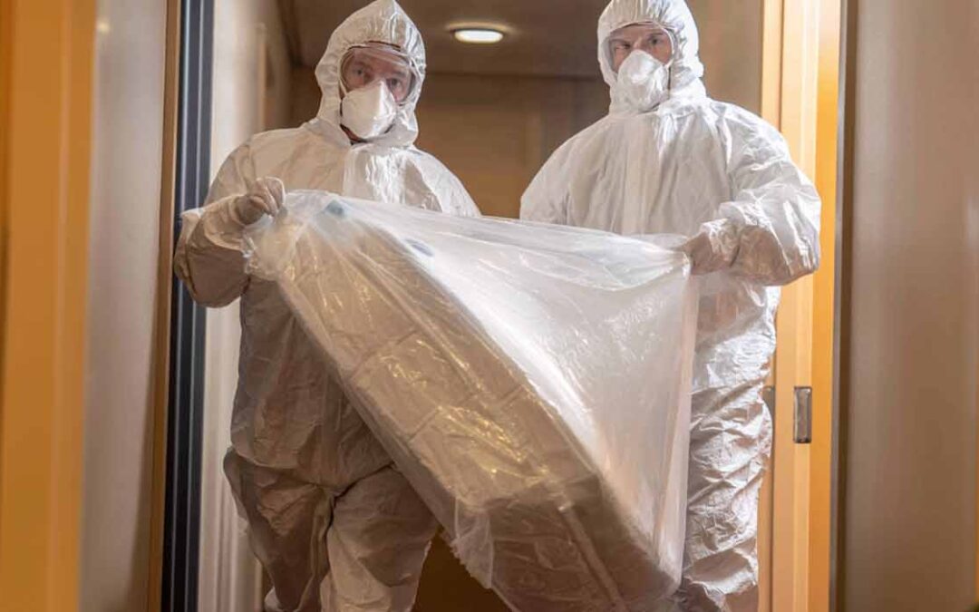 2 biohazard technicians carrying a mattress to discard